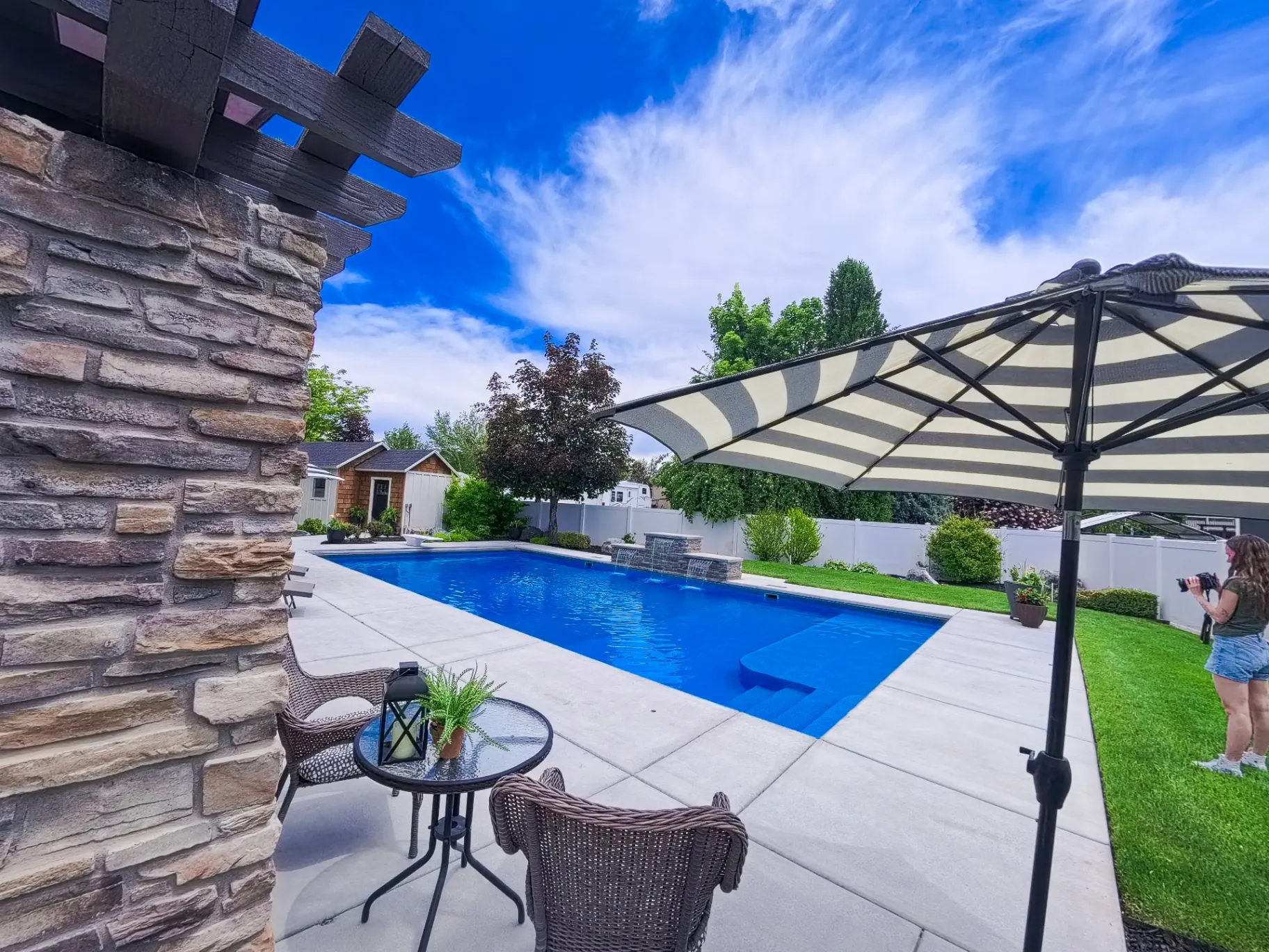 Custom vinyl swimming pool with stone pergola, waterfall feature and expansive patio in Farmington, Utah by Barr Pool Builders