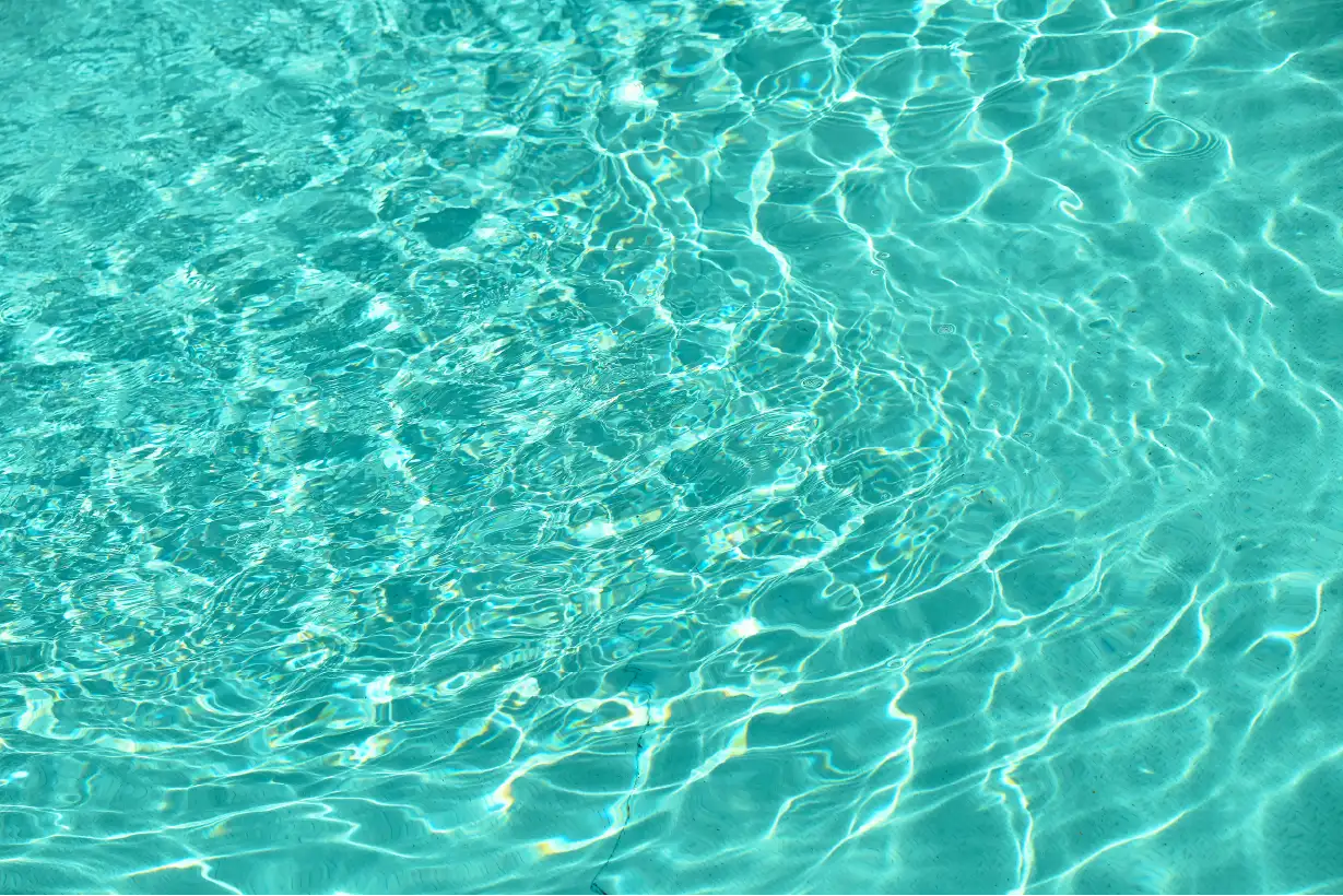 Crystal clear teal-blue vinyl swimming pool freshly opened for spring in a Northern Utah backyard with clean water, skimmer, and pool cover removed