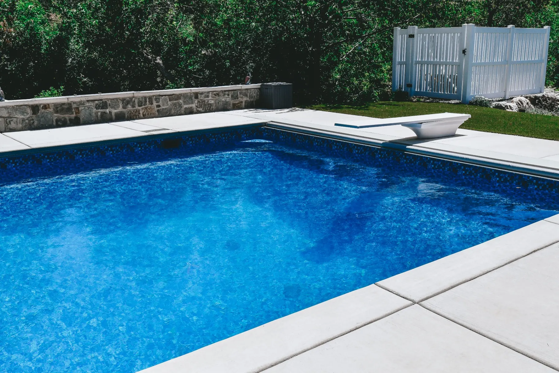 Blue mosaic-tile vinyl liner swimming pool with diving board and concrete deck in Kaysville, Utah by Barr Pool Builders