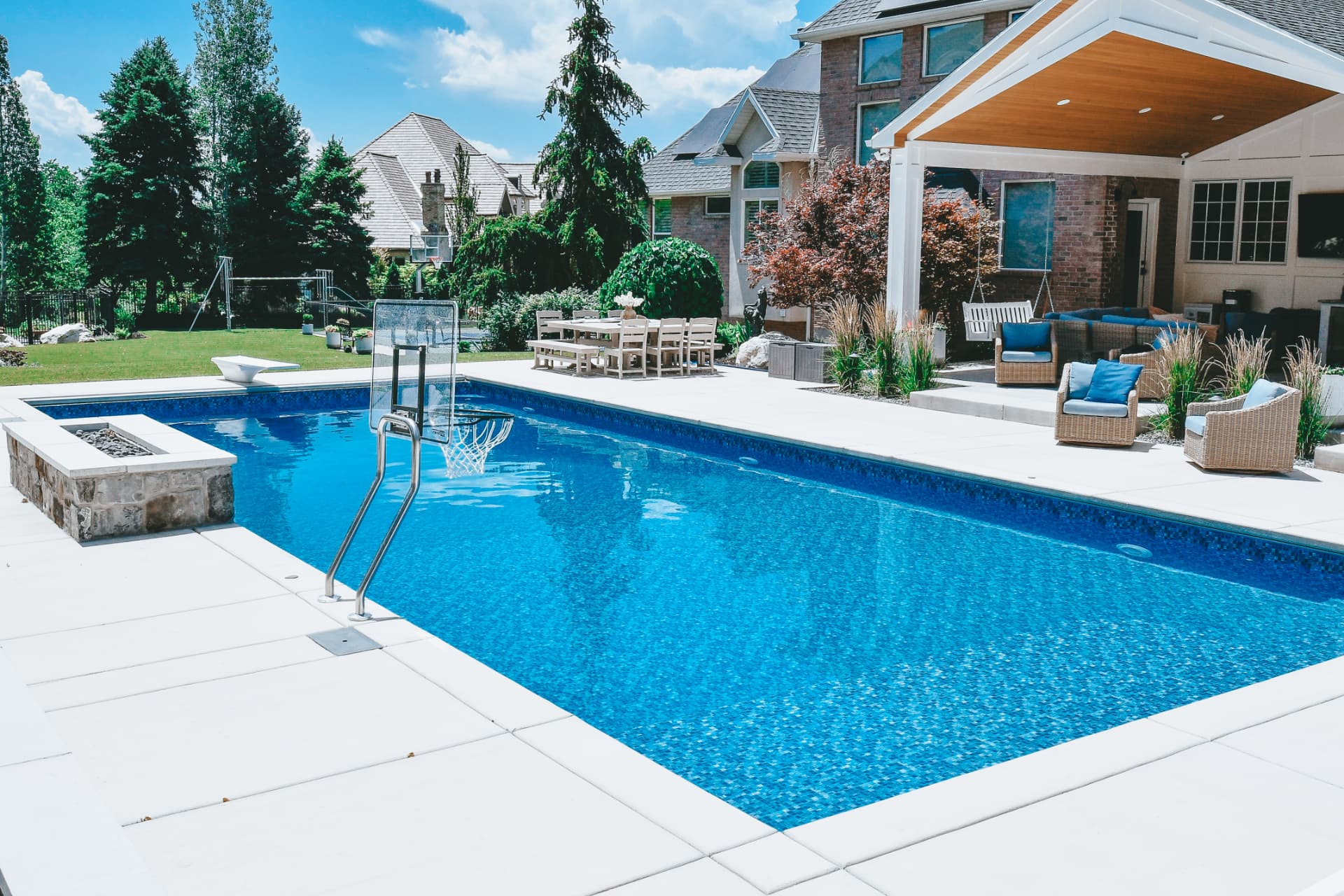 Luxury vinyl inground swimming pool with in-pool basketball hoop, stone firepit, diving board and covered pavilion lounge in a Farmington, Utah estate by Barr Pool Builders