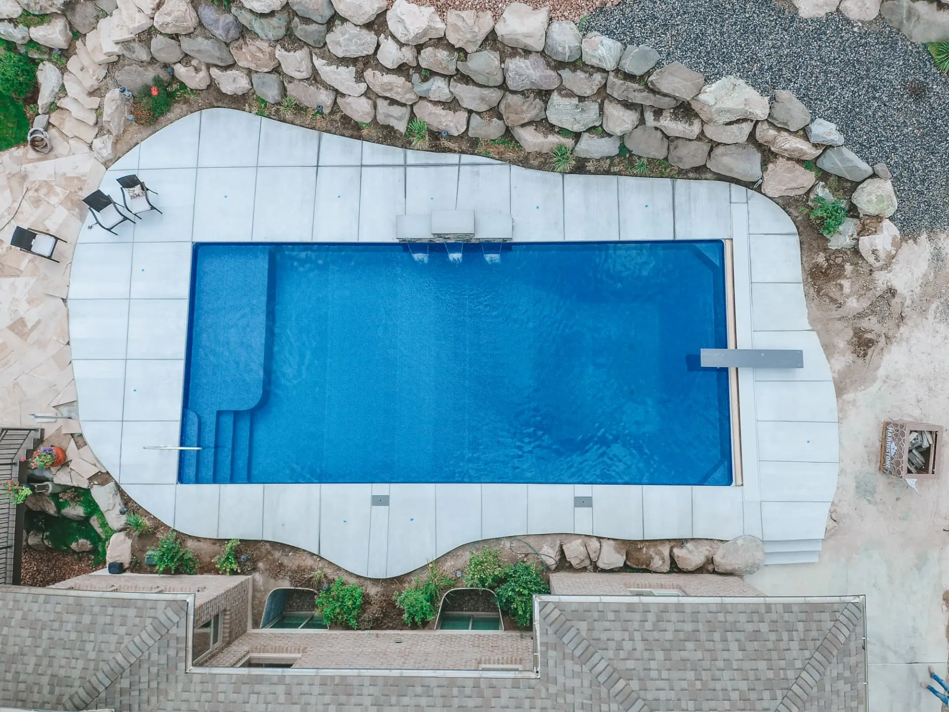 Aerial drone view of a modern rectangle vinyl inground swimming pool with tanning ledge, diving board and freeform stone patio in Ogden, Utah by Barr Pool Builders