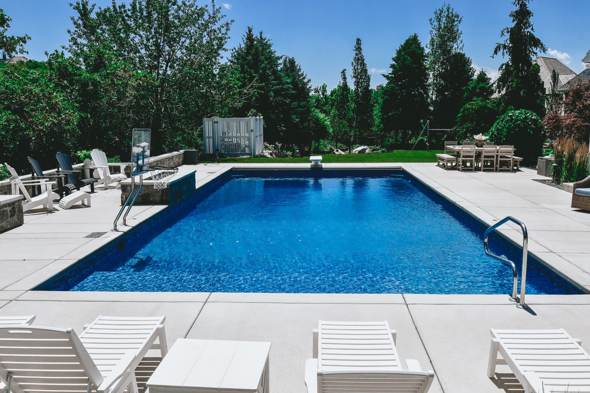 Rectangle vinyl inground swimming pool with in-pool basketball hoop, Adirondack chairs and white lounge seating in a Kaysville, Utah backyard by Barr Pool Builders