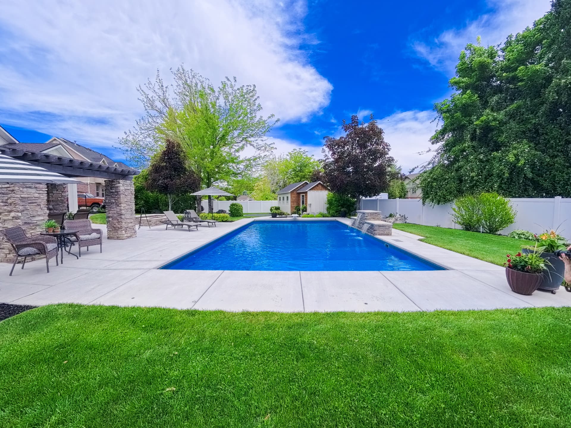 Rectangle vinyl inground swimming pool with stone pergola, striped umbrella lounge and cascading water features in a Syracuse, Utah backyard by Barr Pool Builders
